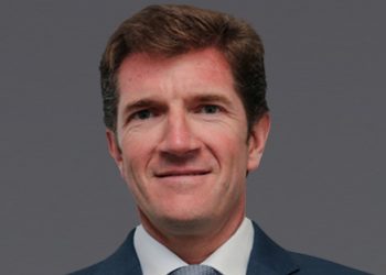 Portrait of a middle-aged man in a navy suit and light blue tie against a gray background, smiling subtly.
