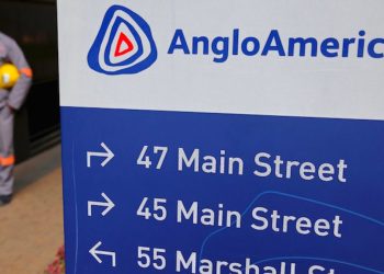 ANGLOAMERICAN | Mining and Energy Namibia | Namibia’s Leading Mining & Energy News Signboard with AngloAmerican logo and arrows to 47 Main Street, 45 Main Street, and 55 Marshall Street; worker in gray uniform holding a yellow helmet in the background.