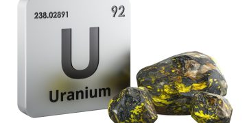 Uranium element tile with symbol U, atomic number 92, beside yellow-green uranium ore rocks