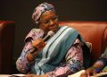 Woman in colorful traditional attire speaking into a handheld microphone at a panel discussion.