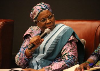 Woman in colorful traditional attire speaking into a handheld microphone at a panel discussion.