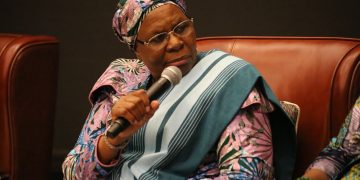 Woman in colorful traditional attire speaking into a handheld microphone at a panel discussion.
