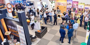 Busy expo hall with numerous booths and attendees networking at a mining conference, colorful displays and lounge area visible.