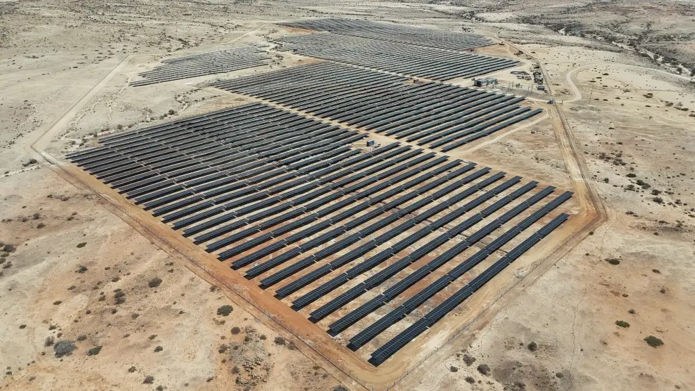 anirep | Mining and Energy Namibia | Namibia’s Leading Mining & Energy News A large solar farm with rows of dark solar panels in a desert landscape from an aerial view.