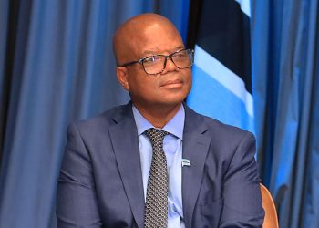 Moeti Mohwasa | Mining and Energy Namibia | Namibia’s Leading Mining & Energy News Man in a navy suit and glasses sits on stage with a blue curtain backdrop.