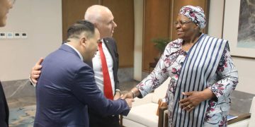 WhatsApp Image 2026-07-18 at 83102 AM | Mining and Energy Namibia | Namibia’s Leading Mining & Energy News Two men in suits greet an African woman in a patterned outfit with a warm handshake in a formal lobby setting, smiling faces evident.