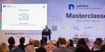 Speaker at a podium on a branded Namibia Oil and Gas Conference stage, presenting to an audience; screen shows Rhino Resources logo and 'Special Address'.