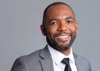 Pinehas Mutota | Mining and Energy Namibia | Namibia’s Leading Mining & Energy News Professional headshot of a smiling man in a gray suit, white shirt, and black tie against a light gray background.