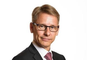 Professional headshot of a middle-aged man in a dark suit and red tie, wearing glasses, looking at the camera.