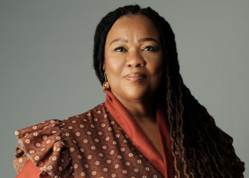 ZENZIE AWASES | Mining and Energy Namibia | Namibia’s Leading Mining & Energy News Portrait of a confident woman with long braids, wearing an orange-brown patterned top, looking at the camera.