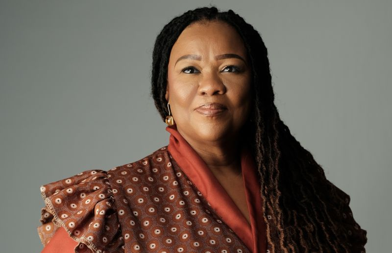 ZENZIE AWASES | Mining and Energy Namibia | Namibia’s Leading Mining & Energy News Portrait of a confident woman with long braids, wearing an orange-brown patterned top, looking at the camera.