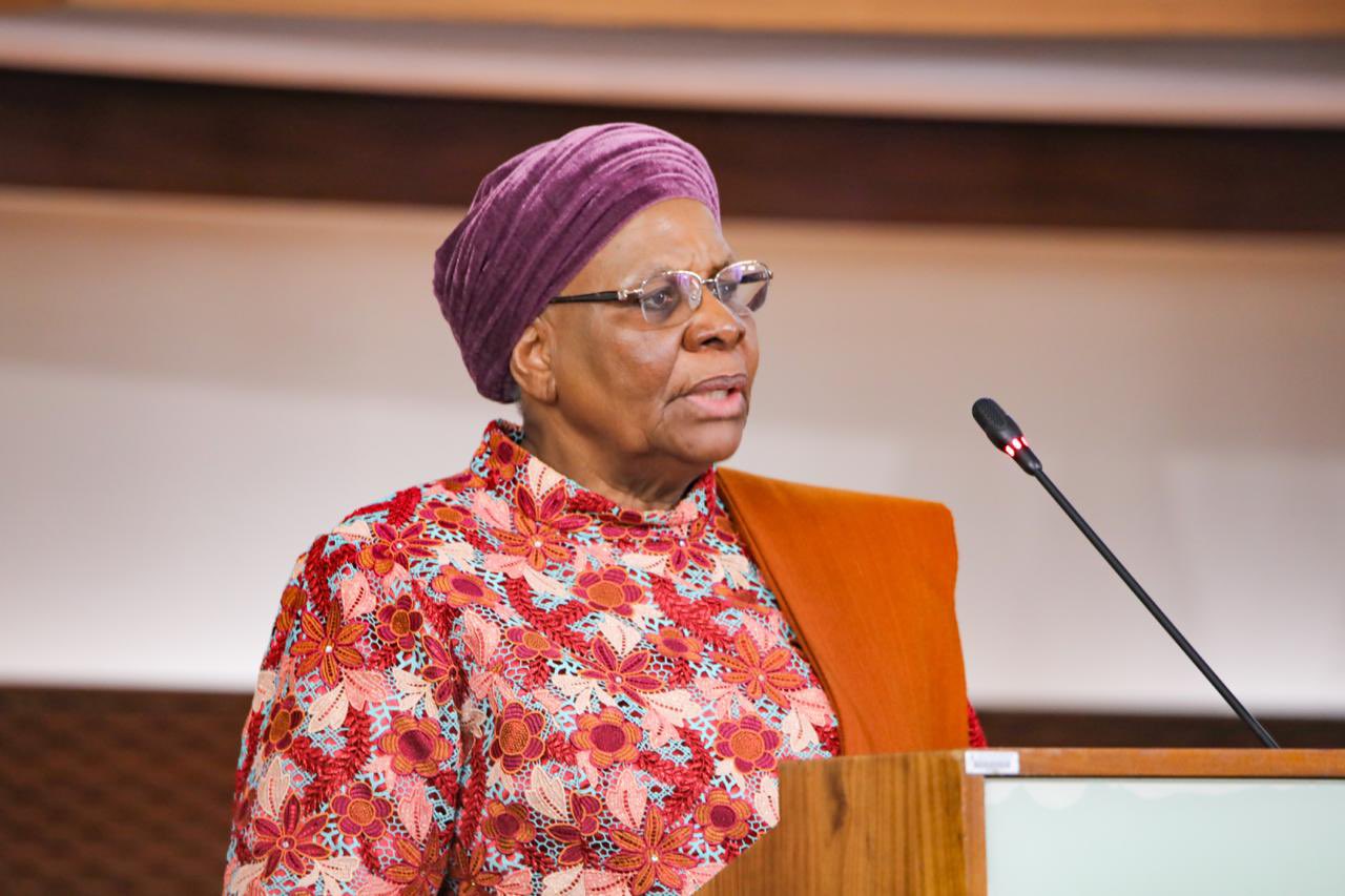WhatsApp Image 2026-08-05 at 10539 PM | Mining and Energy Namibia | Namibia’s Leading Mining & Energy News Older woman with a purple head wrap and floral dress speaks at a wooden podium with a microphone.