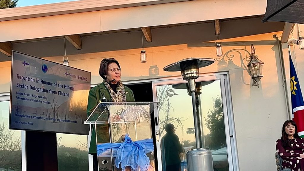 WhatsApp Image 2026-08-07 at 113449 AM | Mining and Energy Namibia | Namibia’s Leading Mining & Energy News Woman in a green blazer speaks at a clear podium on an outdoor terrace, with a screen showing a Finland mining sector event to her left.