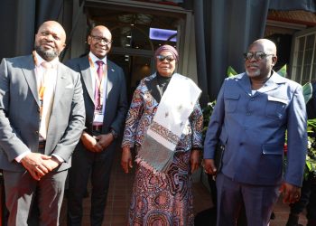 WhatsApp Image 2026-08-08 at 103225 AM | Mining and Energy Namibia | Namibia’s Leading Mining & Energy News Four well-dressed adults posing outside a doorway: two men in suits, a woman in a patterned dress with a headwrap, and a man in a blue uniform; all wearing lanyards.