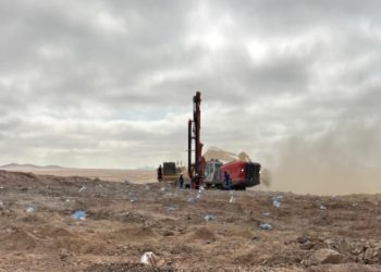 tractor | Mining and Energy Namibia | Namibia’s Leading Mining & Energy News Red drilling rig operates in a dusty, barren desert with a few workers nearby under a cloudy sky