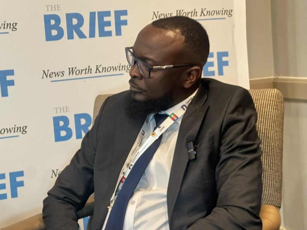 Man in a dark suit and glasses seated in a discussion, with a backdrop that says 'THE BRIEF' and 'News Worth Knowing'.