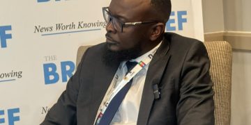 Man in a dark suit and glasses seated in a discussion, with a backdrop that says 'THE BRIEF' and 'News Worth Knowing'.