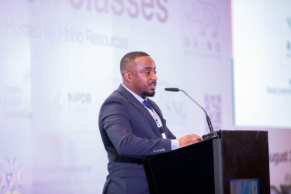 Man in a dark suit speaks at a conference podium with a microphone, facing right.