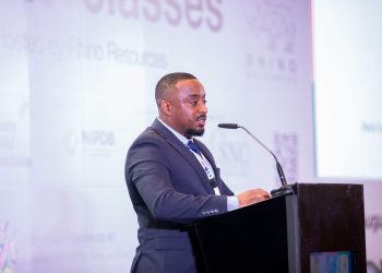 Man in a dark suit speaks at a conference podium with a microphone, facing right.