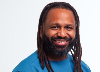 Marco Patrice Victor | Mining and Energy Namibia | Namibia’s Leading Mining & Energy News Smiling man with long dreadlocks and beard wearing a blue shirt, facing the camera against a light background.