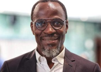 Fillemon Wise | Mining and Energy Namibia | Namibia’s Leading Mining & Energy News Smiling man wearing round glasses, a white shirt, and a dark blazer in a professional setting.