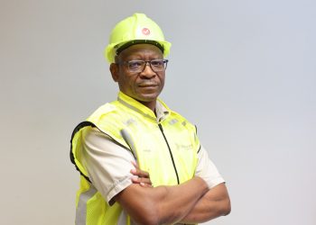 George Botshiwe 4 | Mining and Energy Namibia | Namibia’s Leading Mining & Energy News Construction worker wearing a neon yellow safety helmet and high-visibility vest with arms crossed in front of a neutral background.