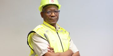 George Botshiwe 4 | Mining and Energy Namibia | Namibia’s Leading Mining & Energy News Construction worker wearing a neon yellow safety helmet and high-visibility vest with arms crossed in front of a neutral background.