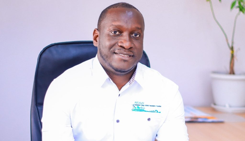 Paulus Mulunga | Mining and Energy Namibia | Namibia’s Leading Mining & Energy News Portrait of a man in a white shirt sitting at a desk, smiling at the camera in an office setting with a plant in the background.
