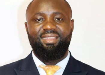 Hasekiel Johannes1 | Mining and Energy Namibia | Namibia’s Leading Mining & Energy News Portrait of a smiling Black man in a navy suit and yellow tie against a light background, a professional headshot.
