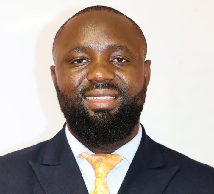 Hasekiel Johannes1 | Mining and Energy Namibia | Namibia’s Leading Mining & Energy News Portrait of a smiling Black man in a navy suit and yellow tie against a light background, a professional headshot.