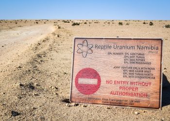 Desert landscape with a large weathered sign reading 'No entry without proper authorisation' for Reptile Uranium Namibia in the foreground.