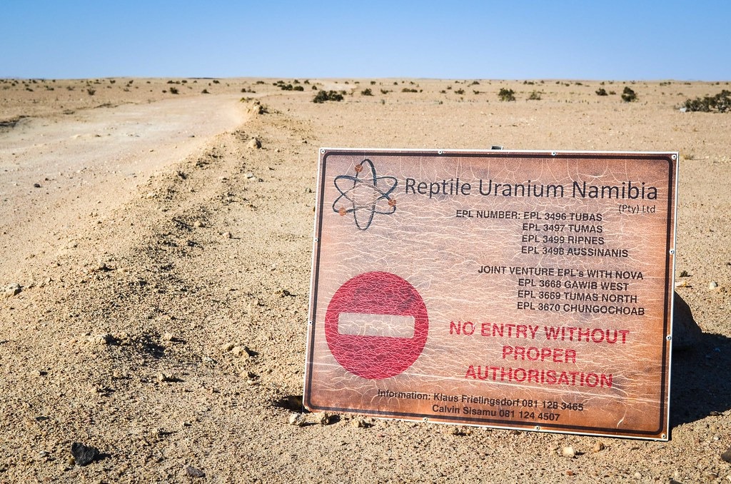 Desert landscape with a large weathered sign reading 'No entry without proper authorisation' for Reptile Uranium Namibia in the foreground.