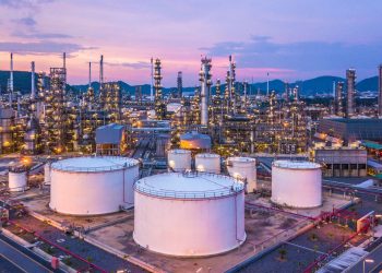 WhatsApp Image 2026-09-06 at 83353 PM | Mining and Energy Namibia | Namibia’s Leading Mining & Energy News Oil refinery at dusk: white storage tanks in foreground and a dense network of pipes and distillation columns under a purple sky with hills in the distance.