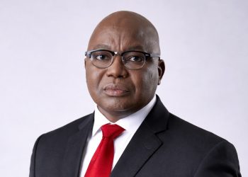 Professional head-and-shoulders portrait of a bald Black man in a black suit and red tie, wearing glasses.