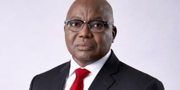 Professional head-and-shoulders portrait of a bald Black man in a black suit and red tie, wearing glasses.