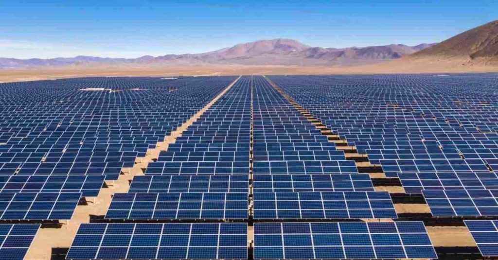 Expansive desert solar farm with rows of blue solar panels stretching to the horizon under a clear blue sky.