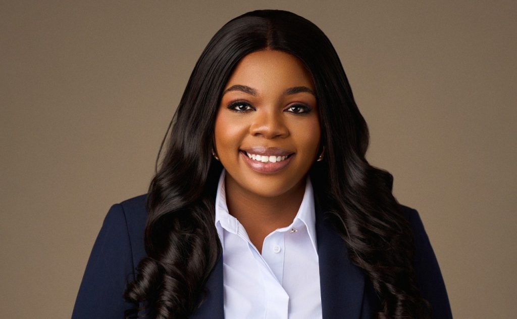Professional headshot of a smiling Black woman with long dark hair in a navy blazer and white shirt.