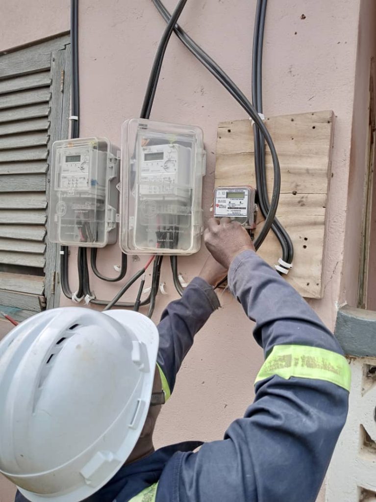 Utility worker wearing a hard hat inspecting outdoor electric meters on a wall