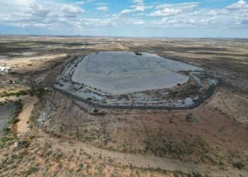 UNICORN RESOURCES | Mining and Energy Namibia | Namibia’s Leading Mining & Energy News Aerial view of a large, flat, light-gray concrete pad encircled by a road in a dry desert landscape.