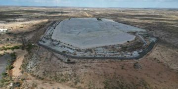 Aerial view of a large, flat, light-gray concrete pad encircled by a road in a dry desert landscape.