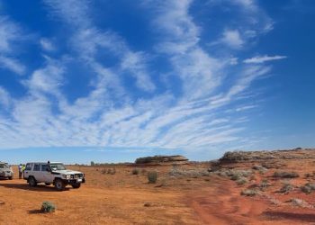 SULTAN RESOURCES | Mining and Energy Namibia | Namibia’s Leading Mining & Energy News Two white off-road vehicles parked on red desert sand under a bright blue sky with wispy clouds, distant rock formations on the horizon.