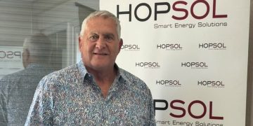 Middle-aged man with gray hair and a patterned shirt posing in front of a HOPSOL banner that reads Smart Energy Solutions: a simple event photo portrait.