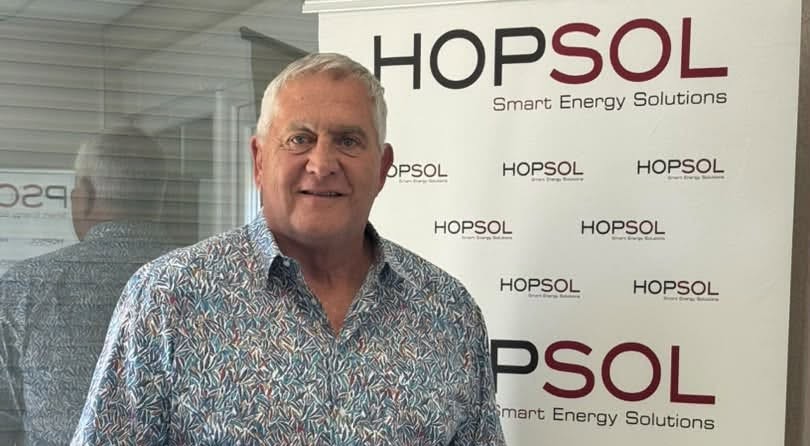 Middle-aged man with gray hair and a patterned shirt posing in front of a HOPSOL banner that reads Smart Energy Solutions: a simple event photo portrait.