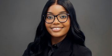 Wetu W Ishitile | Mining and Energy Namibia | Namibia’s Leading Mining & Energy News Professional headshot of a smiling woman with long black hair and glasses, wearing a black blazer against a gray backdrop.