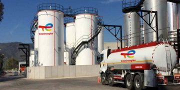 TOTALENERGIES9 | Mining and Energy Namibia | Namibia’s Leading Mining & Energy News Industrial facility with tall white TotalEnergies storage tanks and a branded tanker truck in the foreground under a blue sky with stairs and piping visible.
