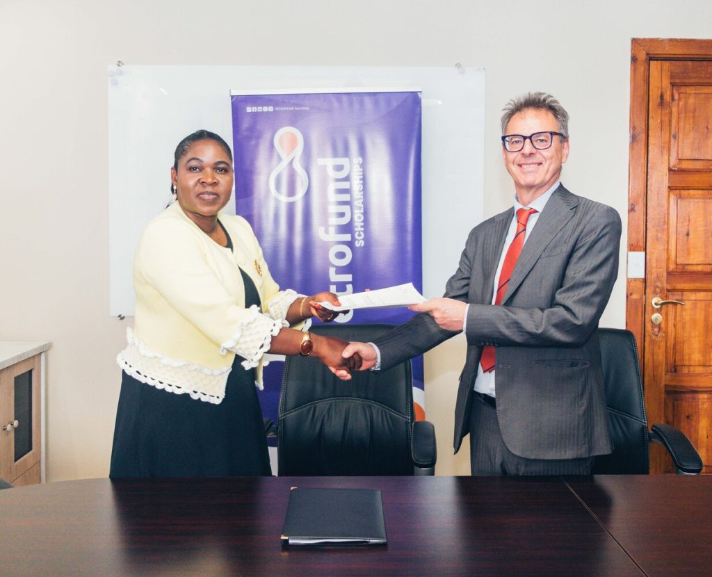 Two professionals shake hands across a dark conference table, exchanging a document in front of a blue banner.