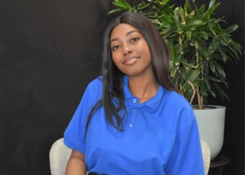 FRANSINA NELULU | Mining and Energy Namibia | Namibia’s Leading Mining & Energy News Young woman with long dark hair in a blue polo shirt, seated indoors with a plant behind her and a black wall backdrop.