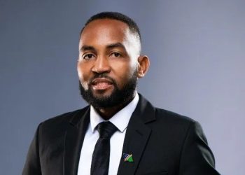 JACKSON NANGOLO | Mining and Energy Namibia | Namibia’s Leading Mining & Energy News Professional headshot of a man in a black suit and tie, with a small flag lapel pin, against a gray gradient backdrop.
