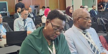 WhatsApp Image 2026-10-06 at 55644 PM | Mining and Energy Namibia | Namibia’s Leading Mining & Energy News Front-row conference attendees: a woman in a green shawl writing with an orange pen, beside a man in a light gray suit and glasses.