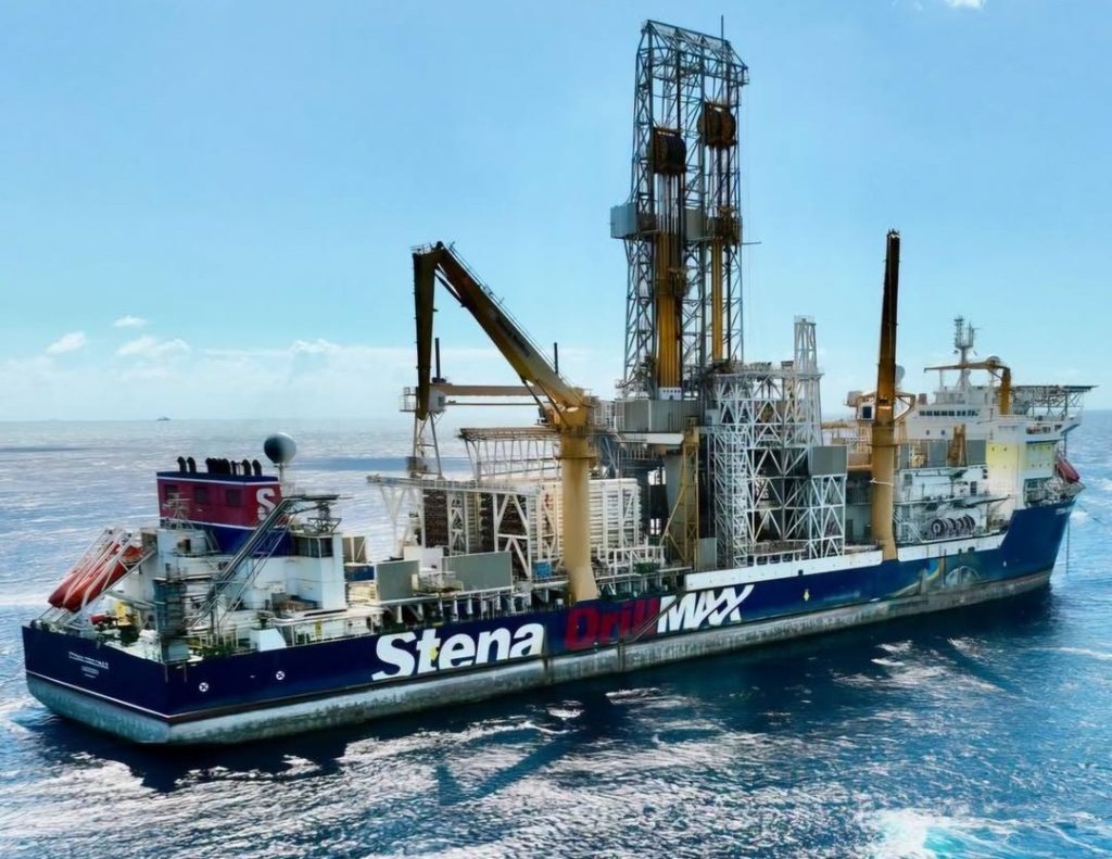 Offshore drilling ship at sea, blue hull with 'Stena Drilling' branding and tall yellow derricks towering above.